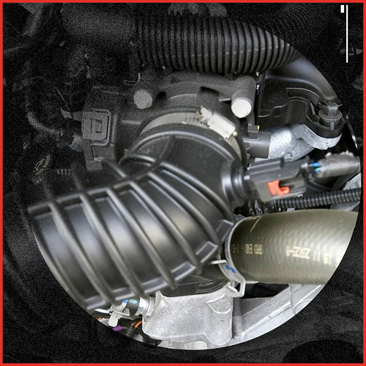 Nahaufnahme eines Motorteils. Ein schwarzes, gewelltes Rohr und weitere Fahrzeugteile mit Kabeln und Schläuchen.